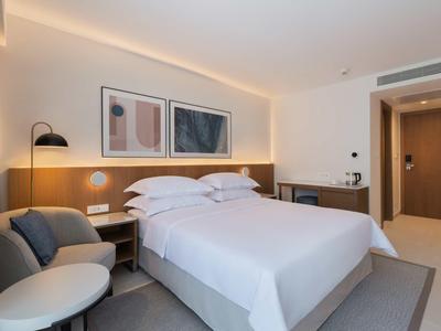 Modern hotel room with large bed, sofa, artwork on wall, and soft lighting.