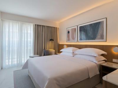 Bright hotel room with double bed, artwork on wall, and large windows with curtains.