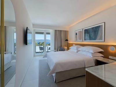 Bright hotel room with double bed, modern design, and sea view through the window.