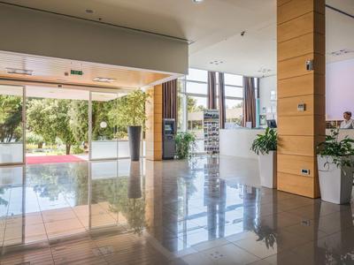 Bright hotel lobby area with large windows, plants, and shiny floor.