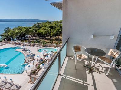 Balcony with table and chairs overlooking a pool and the sea in the background.