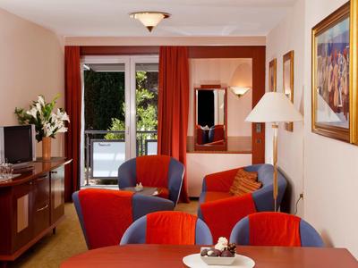 Cozy living room with red armchairs, table, TV, and balcony access.