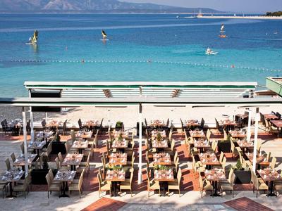 Beach bar with numerous loungers and umbrellas by calm blue sea and mountains in the background.