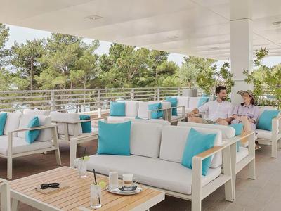 Moderne Außenlounge mit weißen Sofas und blauen Kissen, umgeben von Bäumen auf einer Hotelterrasse.
