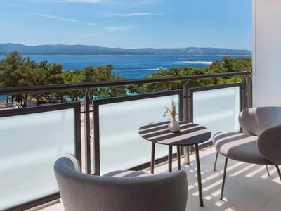 Balkon mit zwei grauen Stühlen und kleinem Tisch mit Blumen mit Blick auf Meer und Hügel.