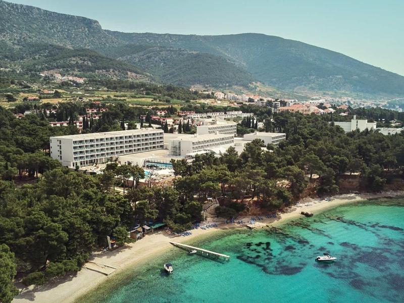Hotel complex along a turquoise coastline with beaches and wooded hills in the background.