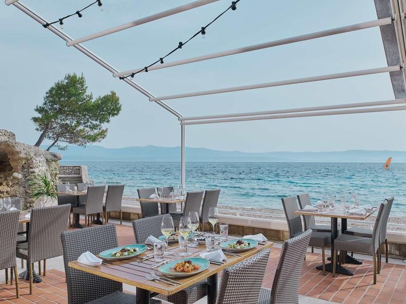 Open-air restaurant overlooking the sea with set tables and comfortable chairs under a pergola.
