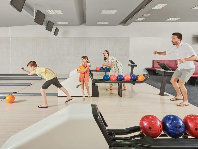 Family playing bowling in a modern bowling alley with colorful balls.