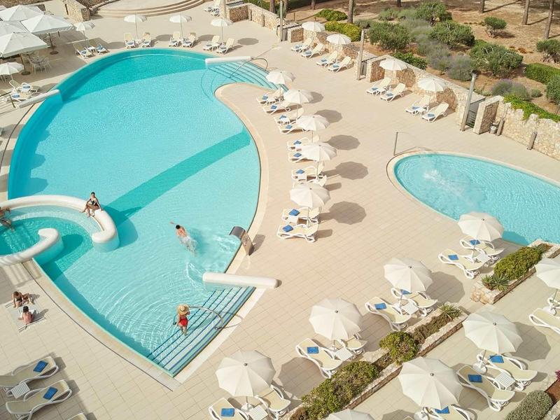 Large hotel pool area with multiple pools, white sun loungers, and umbrellas.