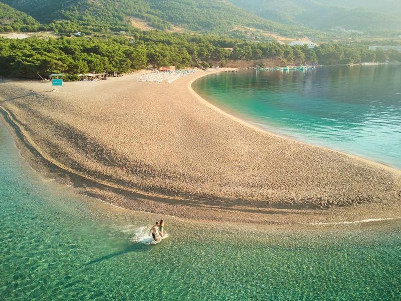 Narrow sandbar with turquoise water and forested hills in the background.
