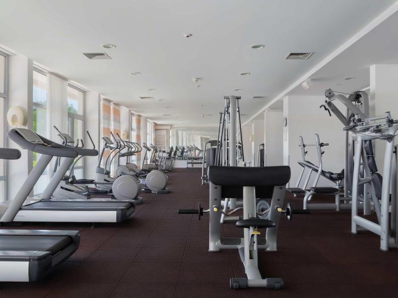 Large gym with treadmills, weights, and modern equipment by large windows.