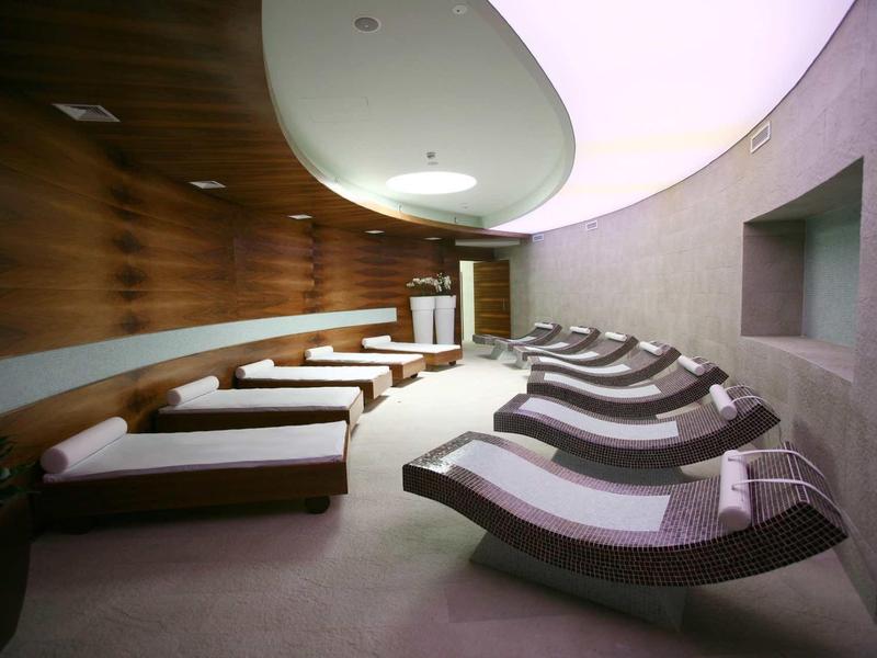 Relaxation room with modern loungers, wood and concrete walls, and indirect ceiling lighting.