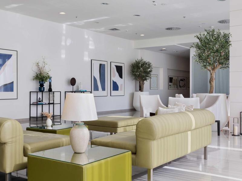 Modern hotel lounge with light sofas, abstract art, and green plants.