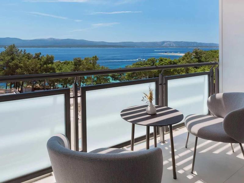 Balcony with two chairs and table overlooking the sea and wooded coastline.