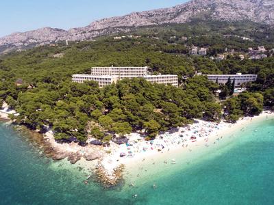 Hotel su una spiaggia boscosa con acqua turchese e montagne sullo sfondo