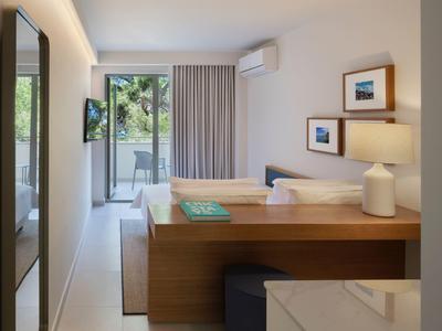 Modern hotel room with double bed, balcony, and desk under natural light.