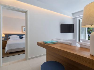 Modern hotel room with desk, TV, and view into an adjacent bedroom.
