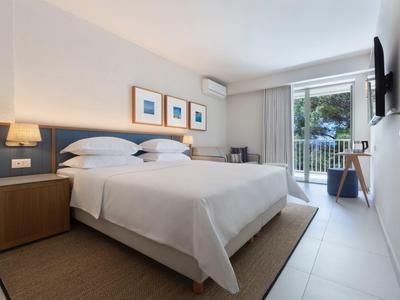 Bright hotel room with double bed, balcony, and simple modern decor.