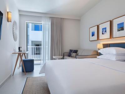 Modern hotel room with double bed, seating area, and balcony with view.