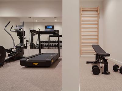 Kleiner Trainingsraum mit Laufband, Hantelbank und Gewichten in neutralen Farben.