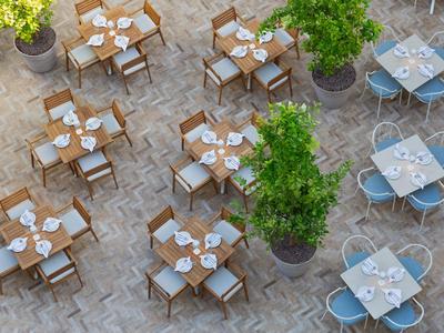 Außenbereich eines Hotels mit mehreren gedeckten Tischen und Stühlen auf gepflastertem Boden.