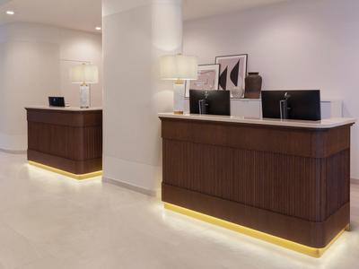 Modern hotel reception with two dark wood desks and bright lighting.