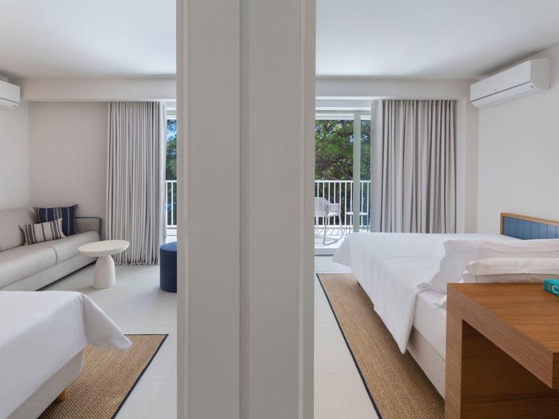 Two modern hotel rooms with beds, seating areas, and balconies overlooking greenery.