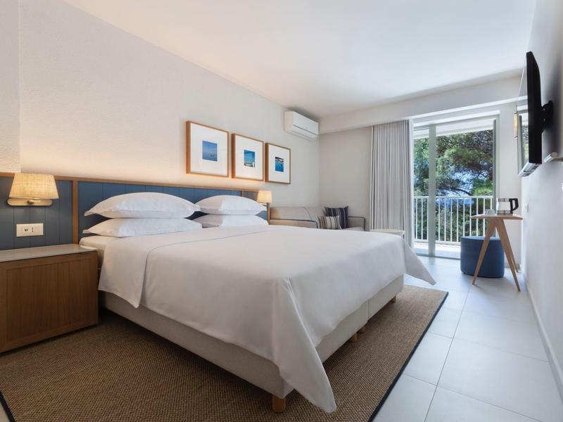 Bright hotel room with double bed, balcony, and simple modern decor.