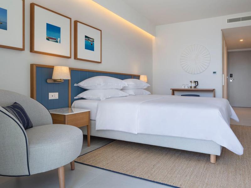 Modern hotel room with double bed, armchair, and minimalist decor.