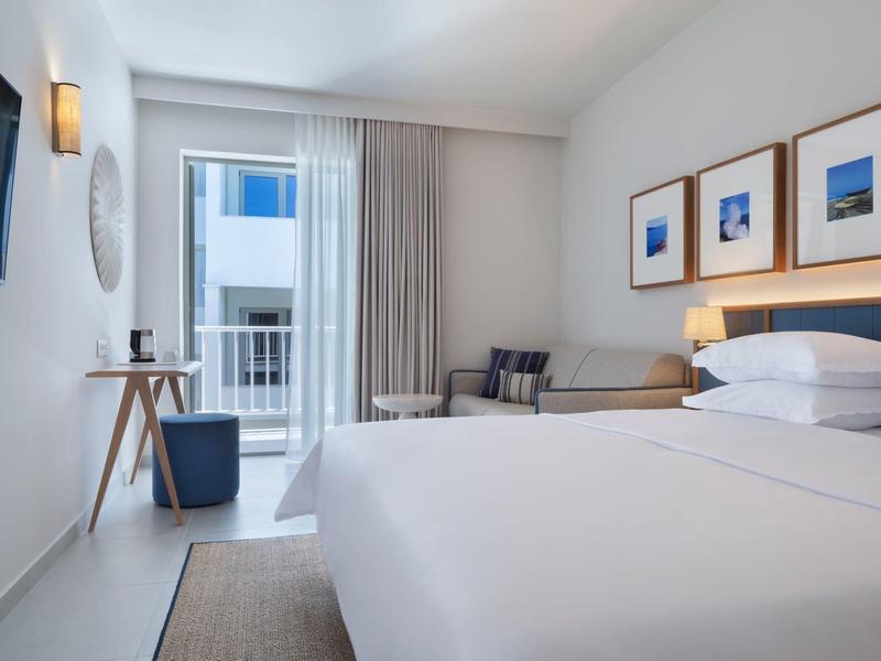 Modern hotel room with double bed, seating area, and balcony with view.