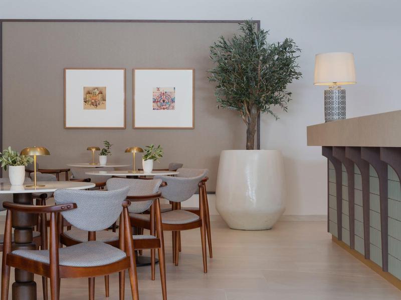 Modern dining room with wooden tables, chairs, plants, and wall art in a hotel.