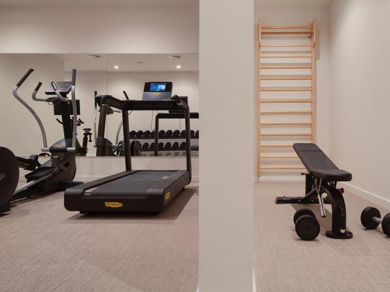 Modern gym with treadmill, workout bench, and dumbbells in a neutral-colored room.