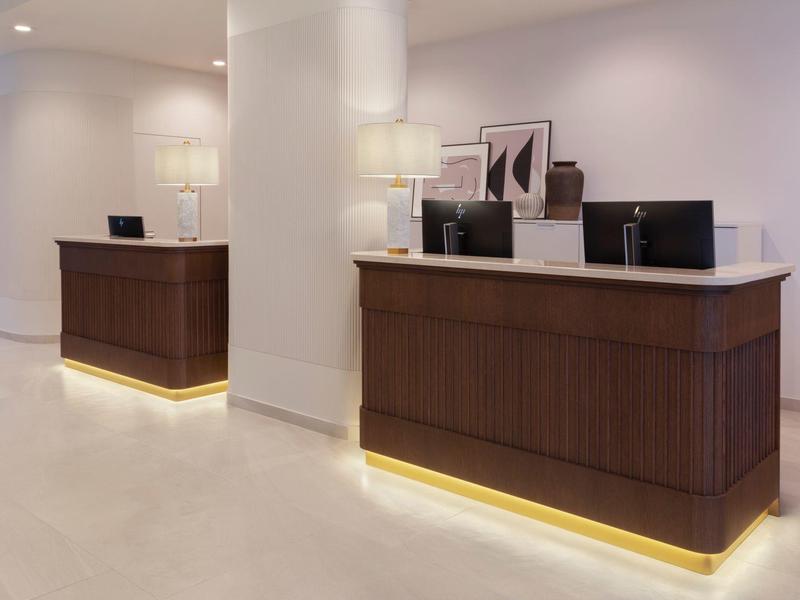 Modern hotel reception with two dark wood desks and bright lighting.