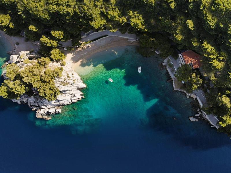 Aerial view of a coastline with clear blue water, sandy beach, and forested shore.