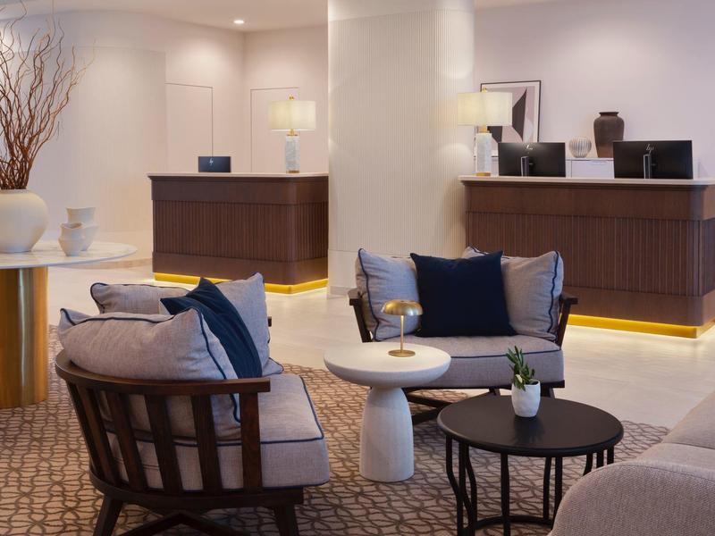 Elegant hotel lounge area with comfortable chairs, tables, and a stylish reception in the background.