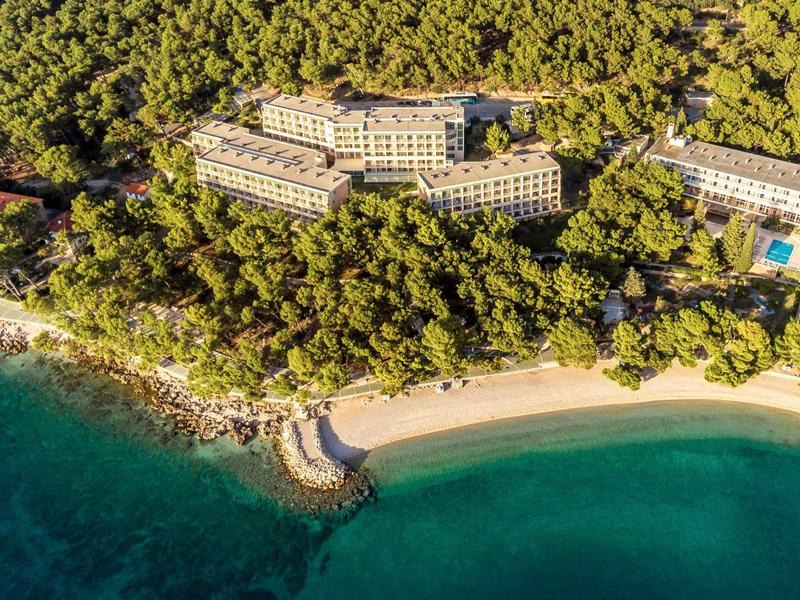 Aerial view of a beachfront hotel surrounded by dense greenery and clear blue water.