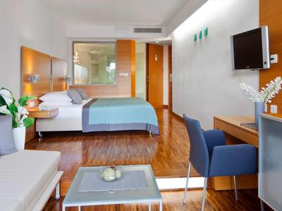 Helles Hotelzimmer mit Doppelbett, Sofa, Schreibtisch, Stühlen und Wand-TV.