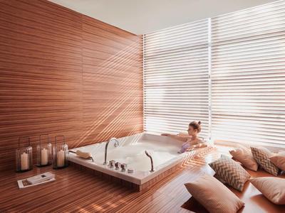 Moderner Holzraum mit eingebautem Whirlpool, Kerzen und bequemen Kissen am Fenster.