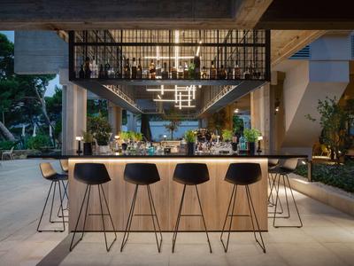 Moderne Outdoor-Bar mit hellem Holz, schwarzen Barhockern und stilvoller Beleuchtung bei Abenddämmerung.