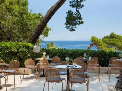 Leere Terrasse mit runden Tischen und Stühlen, umgeben von grünen Bäumen mit Meerblick.