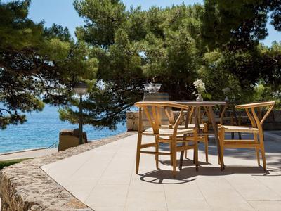 Terrasse mit Holzstühlen und Tisch, umgeben von Pinien, Blick aufs blaue Meer im Hintergrund.
