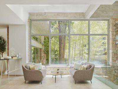 Helles Wohnzimmer mit großen Glasfenstern, zwei grauen Sesseln, Holzsitztisch und Blick ins Grüne.