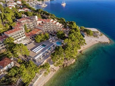 Küstenanlage mit Hotels, viel Grün, Sandstrand und klarem blauem Wasser einer Bucht.