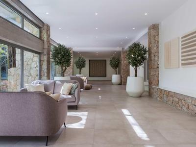 Heller, langer Flur mit großen Pflanzen in weißen Töpfen, beigen Sofas und Natursteinwänden.