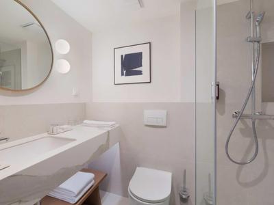 Modernes Badezimmer mit Dusche, Toilette, großem Spiegel und weißen Fliesen.