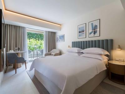 Modernes Hotelzimmer mit Doppelbett, grauem Kopfteil, Schreibtisch, Balkon und neutraler Dekoration.