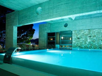 Beleuchteter Poolbereich mit Wasserfontäne und offener Lounge in modernem Design bei Nacht.