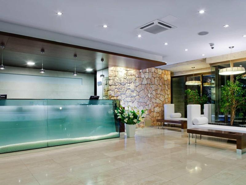 Moderner Empfangsbereich mit Glas-Theke, Steinwand, Pflanzen und minimalistischen Sitzmöbeln.