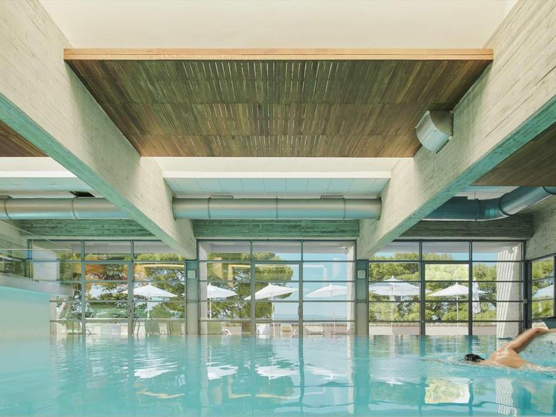 Hallenbad mit großem Fensterfront, Blick auf Außenbereich mit Bäumen und blauem Himmel.