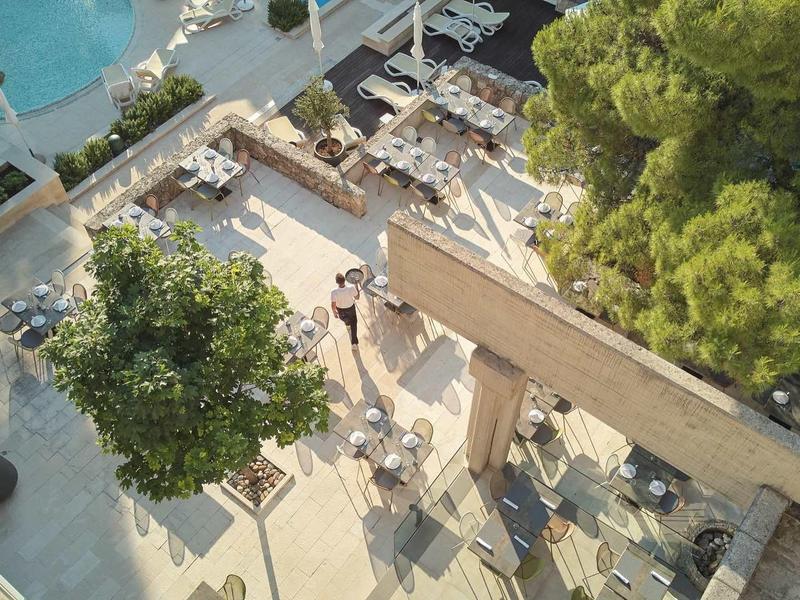 Vogelperspektive auf eine Terrasse mit Tischen, Stühlen, Bäumen und einem angrenzenden Poolbereich.